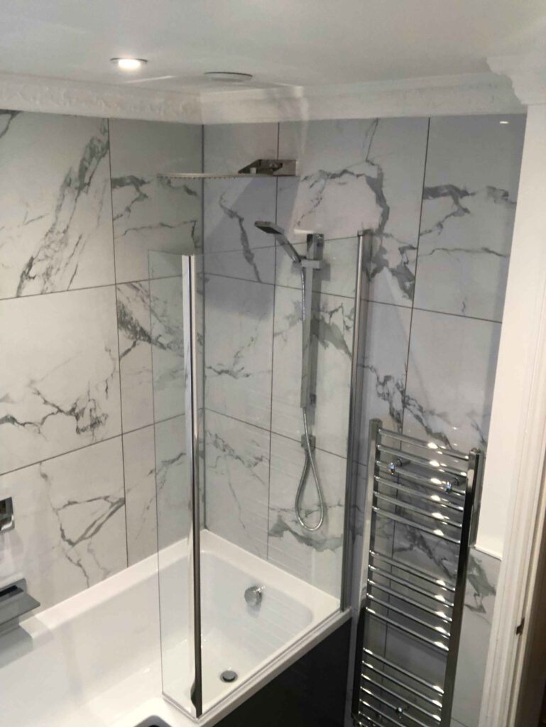 Picture of a bath and shower cubicle with heated towel rail. Light grey tiles with black artistic streaking.