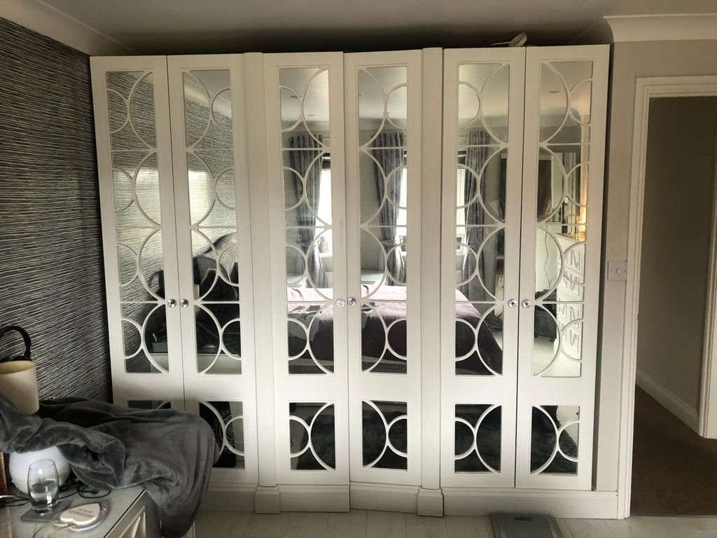 Beautiful custom built bedroom wardrobe. White wood, mirrored door fronts with a wooden swirl effect breaking up the expanse of mirror.
